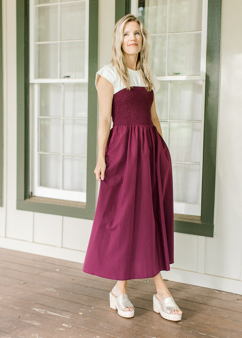 Model wearing a plum midi with a smocked bodice, a white yolk and cap short sleeves. 