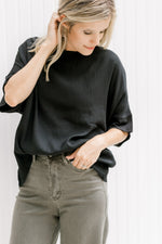 Model wearing a black top with a round neck and short sleeves with a ruffle detail.