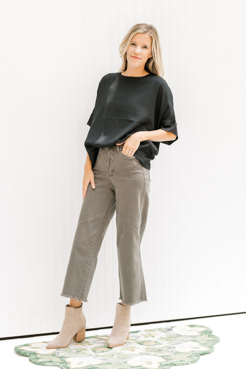 Model wearing gray pants and booties with a black top with short sleeves and a ruffle detail.