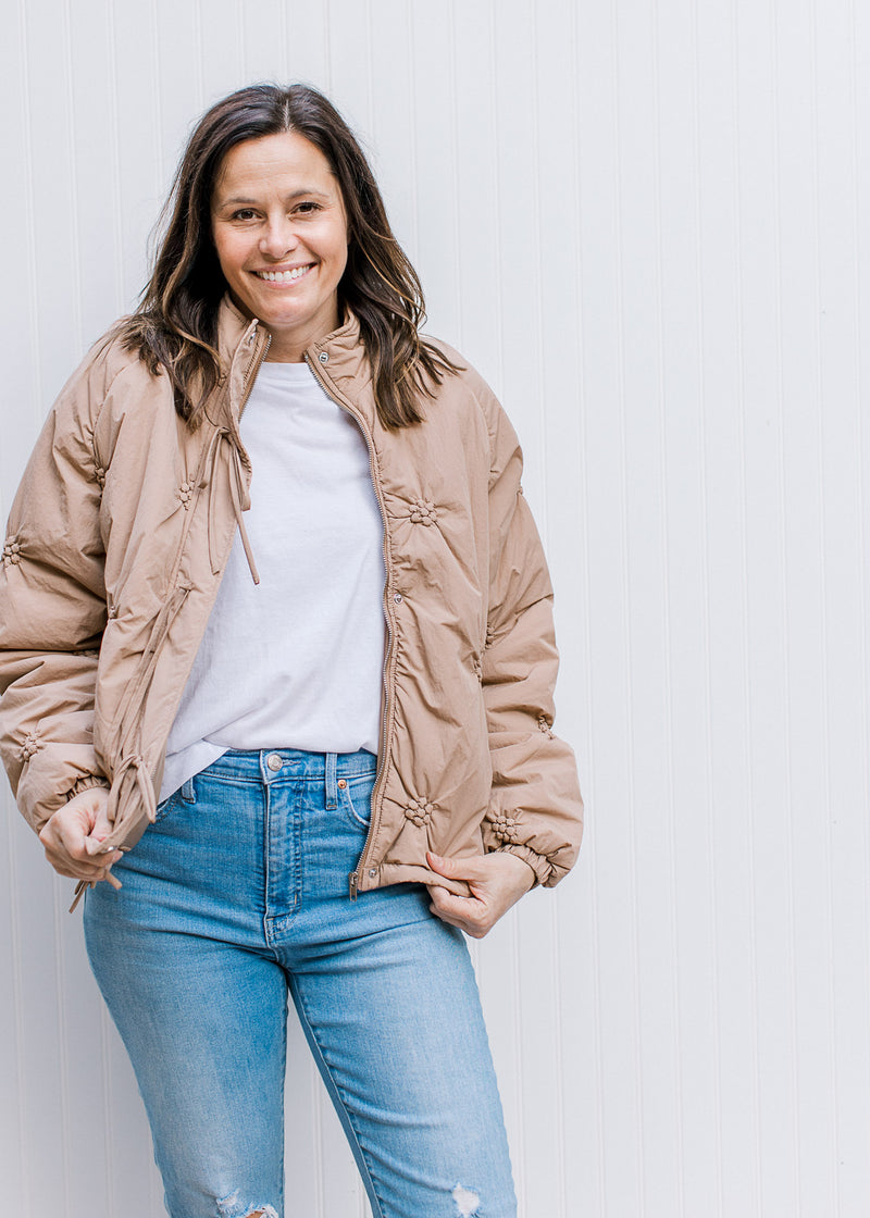 Model wearing a white top with taupe puffer jacket with flower detail and long sleeves.