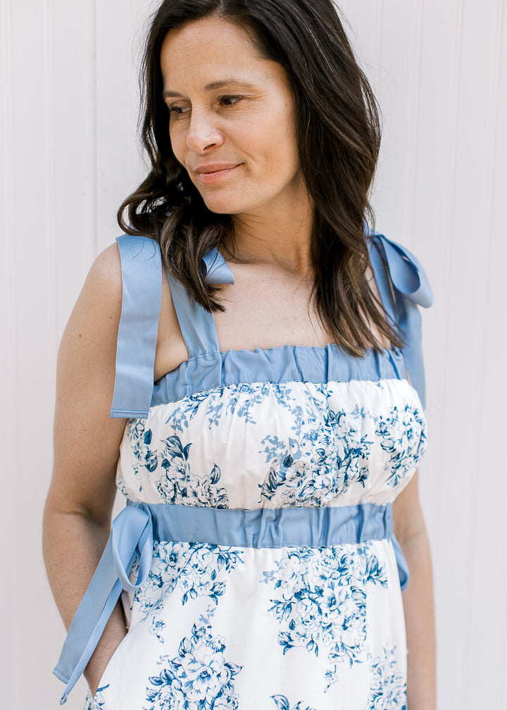 Model wearing a white midi with blue floral, elastic bands at bust and tie spaghetti strap.