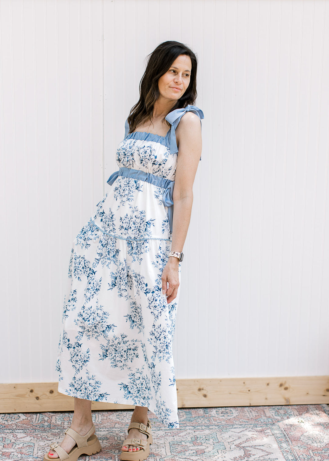 Side view of Model wearing a white midi with blue floral, elastic at bust and tie spaghetti strap.
