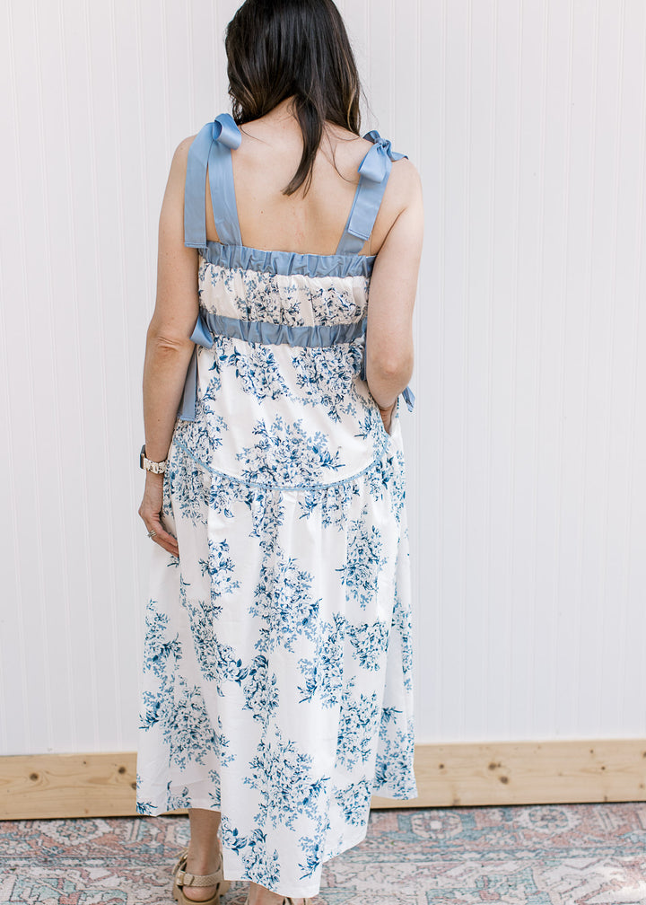 Back view of Model wearing a white midi with blue floral, elastic at bust and tie spaghetti strap.