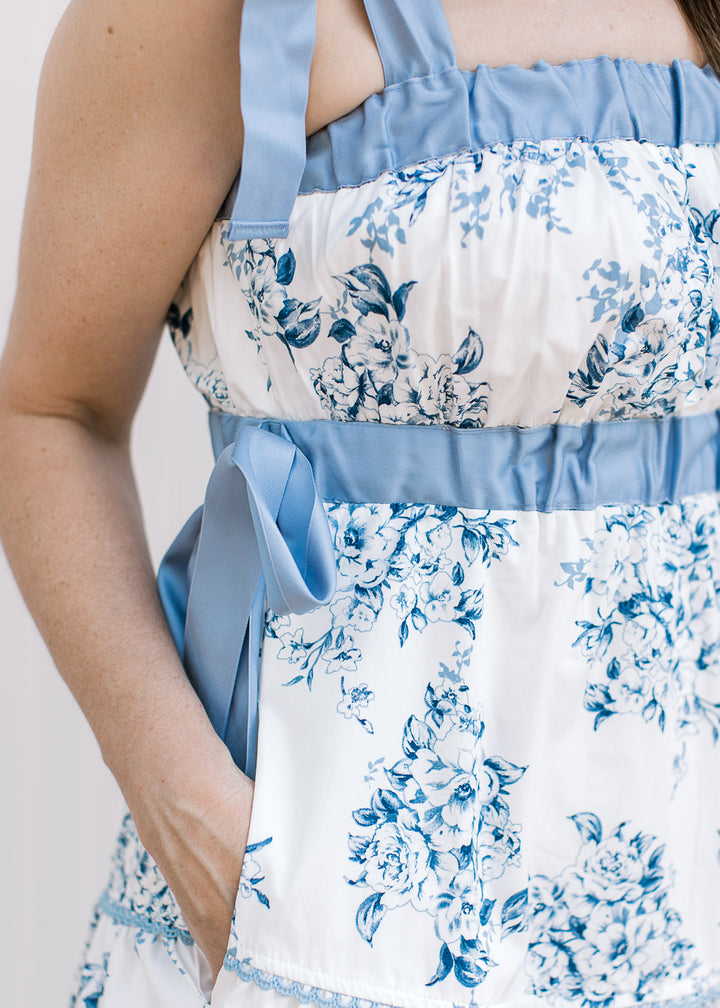 Close up of pockets, elastic at bust and waist with a tie on a white dress with blue floral. 