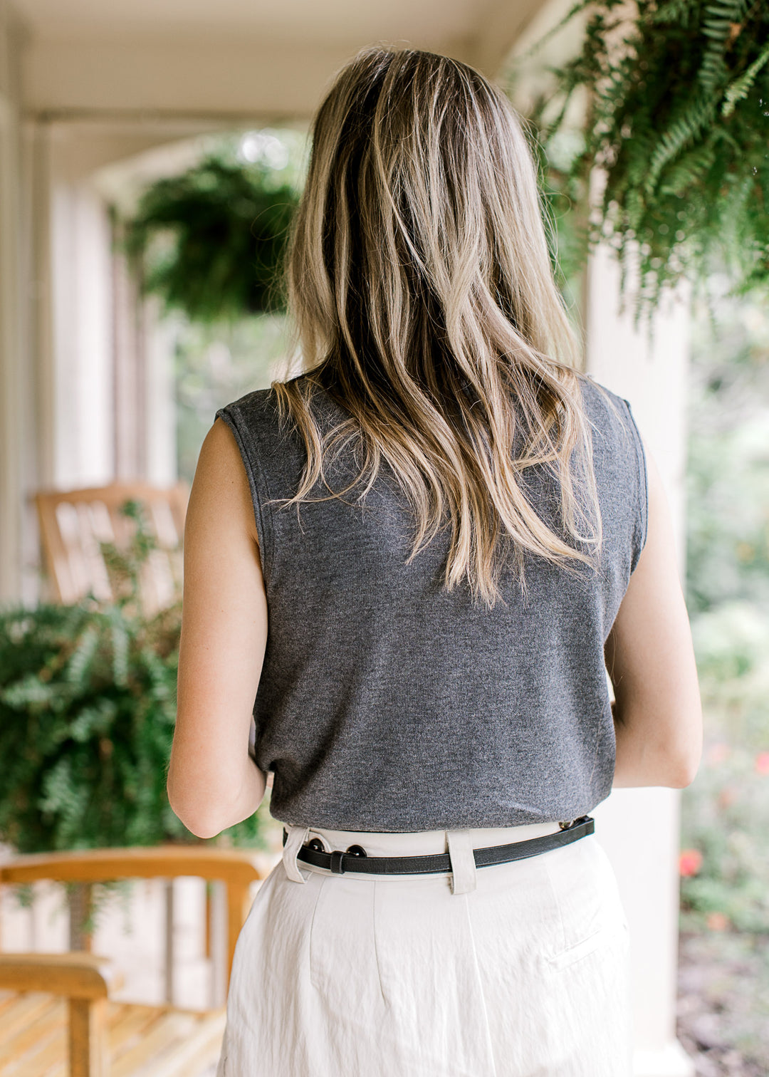 Back view of Model wearing a charcoal sleeveless knit with rolled armholes and button front. 