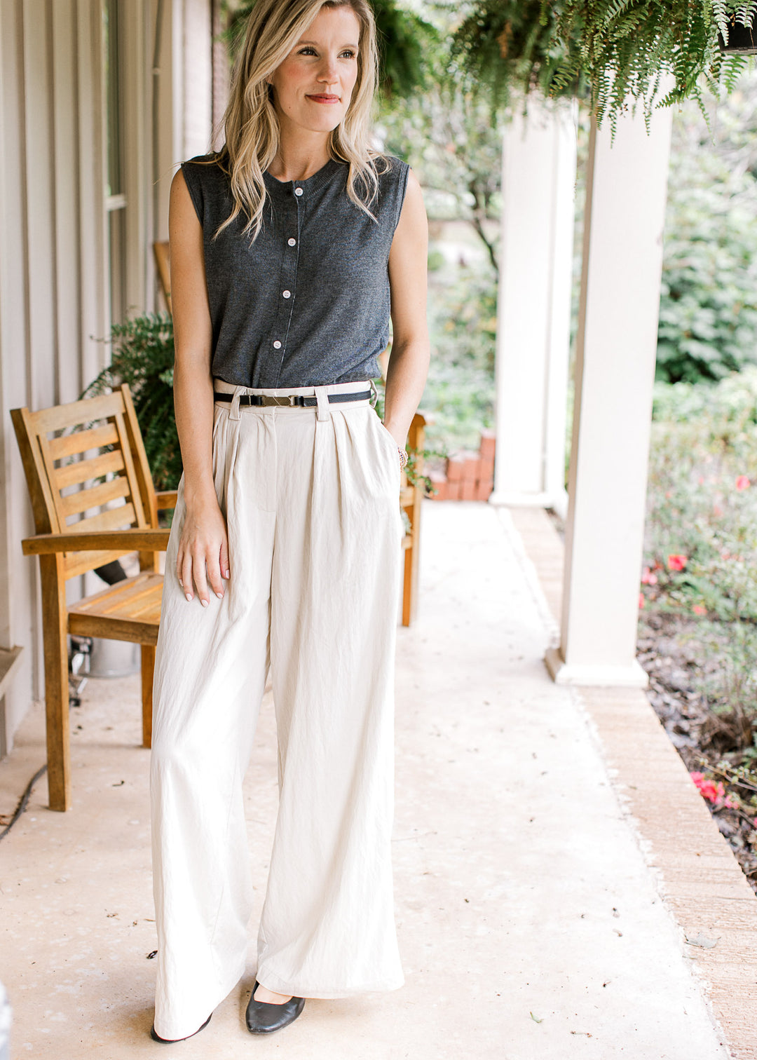 Model wearing white pants and a charcoal sleeveless knit with rolled armholes and button front. 
