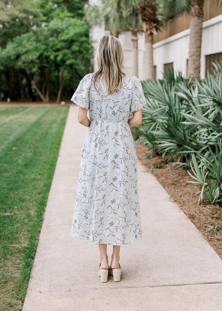 Back view of Model wearing a pale blue midi with cream and navy floral,  v-neck and short sleeves.