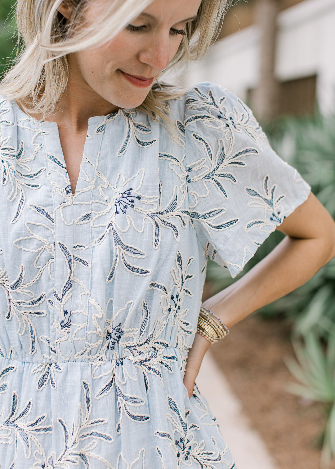 Close up of cream embroidered floral and navy stitching on a pale blue midi with a v-neckline. 