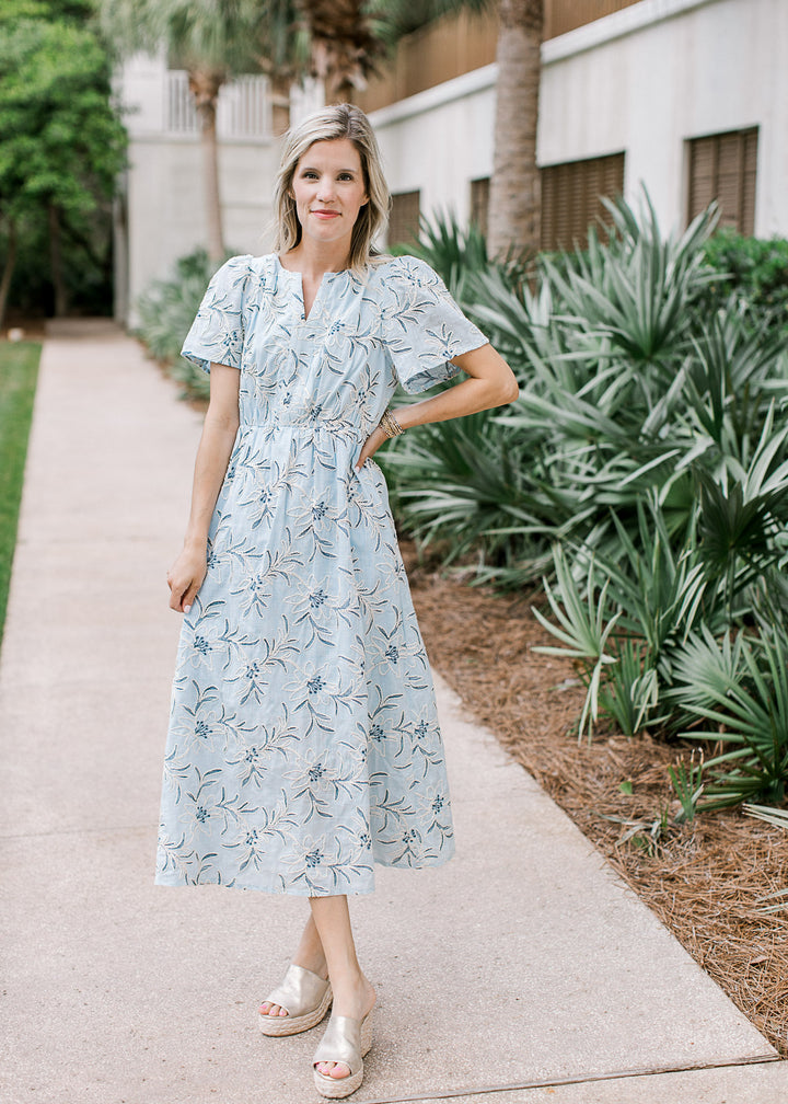 Model wearing a pale blue midi with cream and navy floral,  v-neckline, short sleeves and pockets.