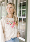 Model wearing a cream top with embroidered flowers, long sleeves and a round neck. 