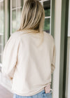 Back view of Model wearing a cream top with embroidered flowers, long sleeves and a round neck. 