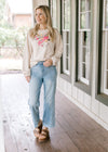 Model wearing jeans, wedged sandals and a cream long sleeve top with embroidered flower.