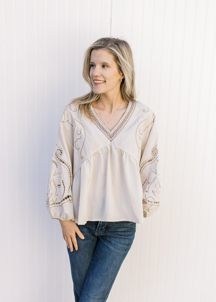 Model wearing a khaki babydoll top with taupe and cream embroidery, v-neck and bubble long sleeves. 