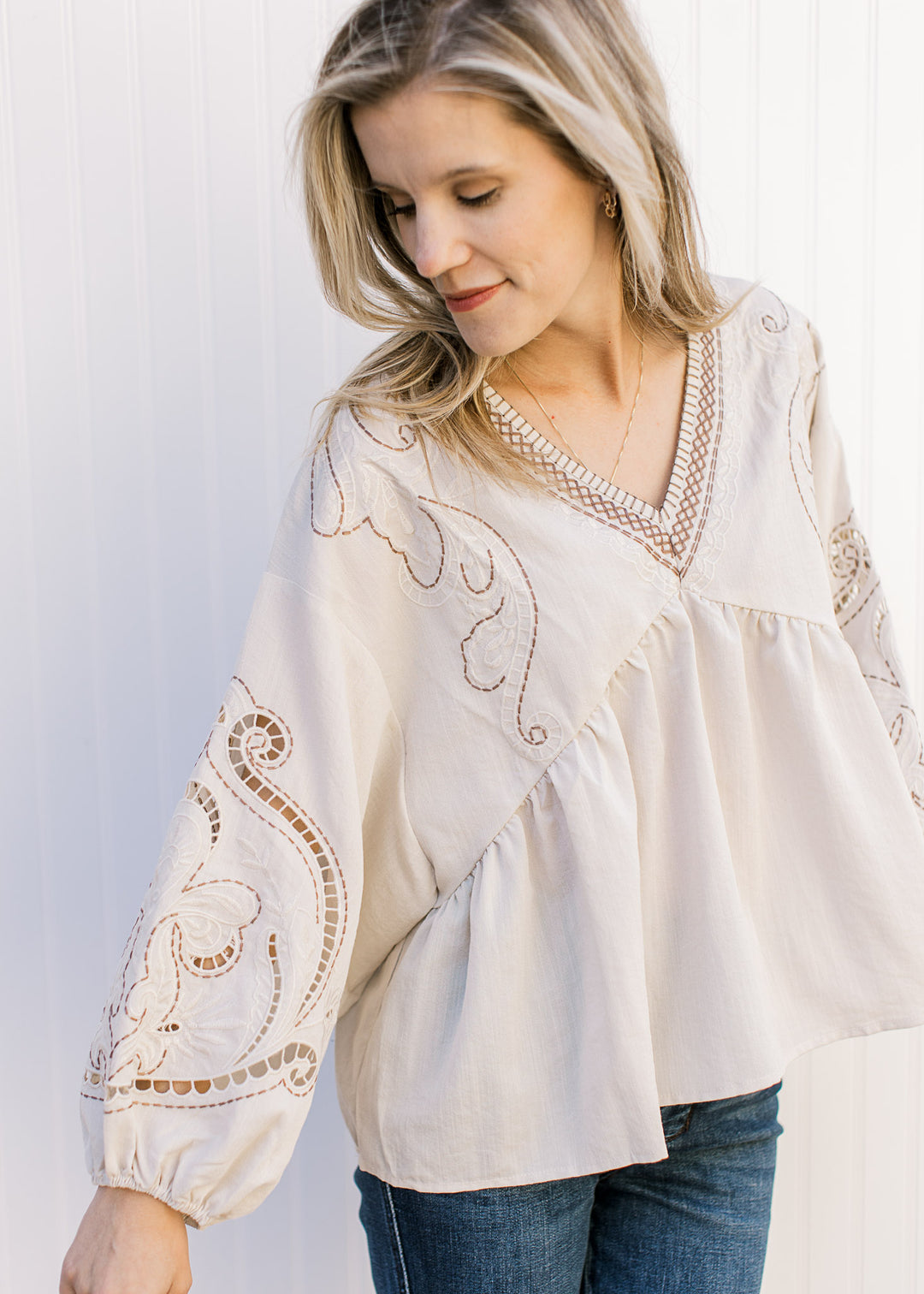 Open stitching on the bubble sleeve of a khaki babydoll top with embroidered detail and a v-neck.  