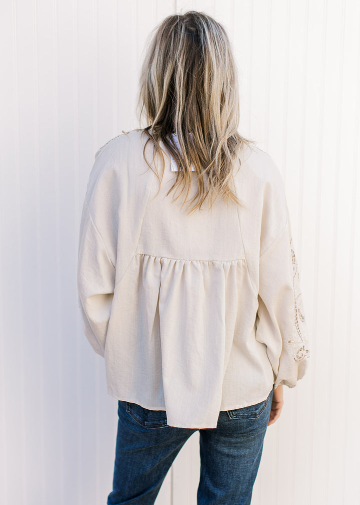 Back view of Model wearing a khaki babydoll top with taupe and cream embroidery. 