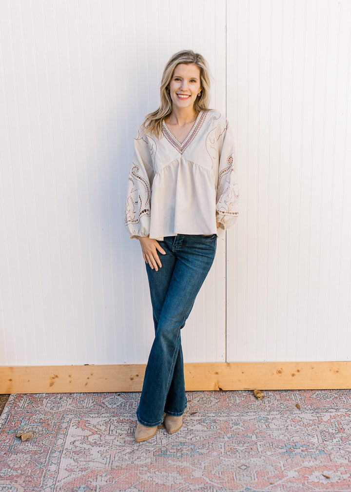 Model wearing jeans and a khaki top with taupe and cream embroidery, v-neck and long sleeves. 