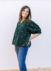 Model wearing jeans and a deep green corduroy top with cream embroidered flowers and a v-neck.  