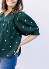 Model wearing a deep green top with cream embroidered flowers and bubble short sleeves.