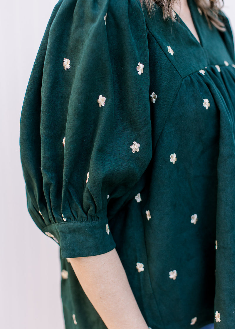 Close up of embroidered cream flowers on a v-neck hunter green top with short bubble sleeves. 