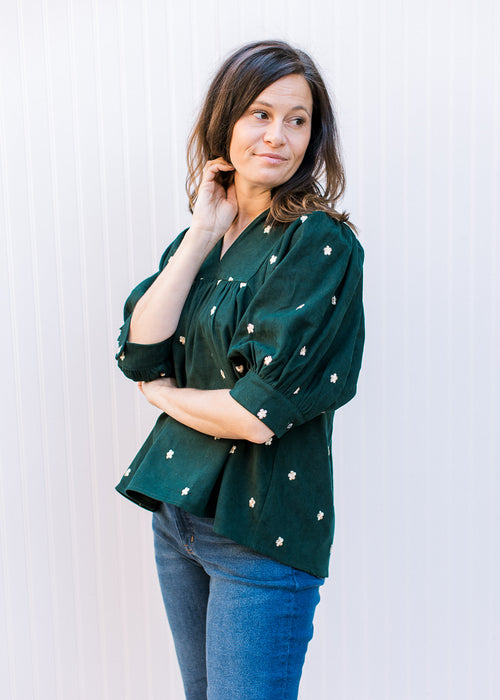 Model wearing a deep green corduroy top with cream embroidered flowers and a v-neck. 