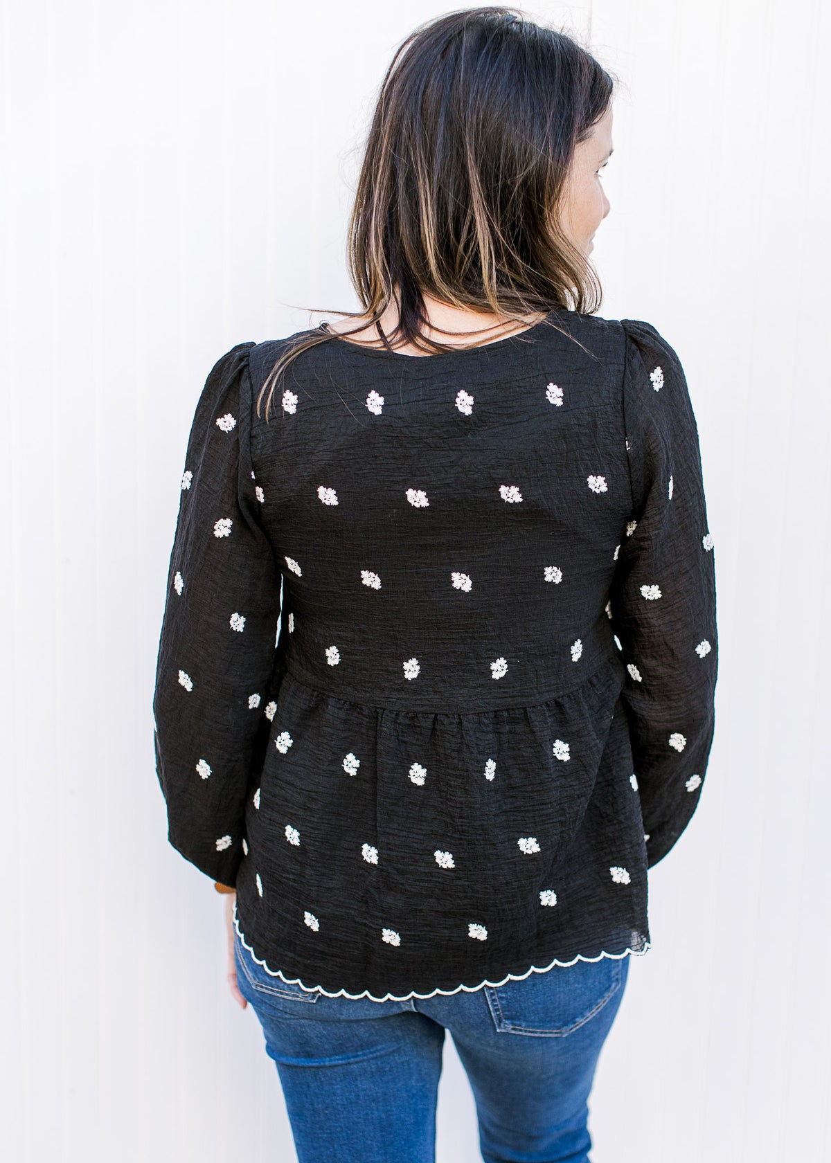 Back view of Model wearing a black top with white embroidered flowers and bubble long sleeves. 