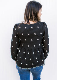 Back view of Model wearing a black top with white embroidered flowers and bubble long sleeves. 