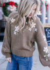 Model wearing an olive green sweater with cream embroidered flowers and bubble long sleeves. 