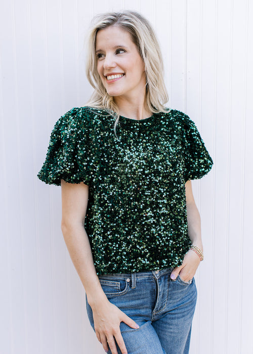 Model wearing an emerald green sequin top with short puff sleeves and pleated shoulders.