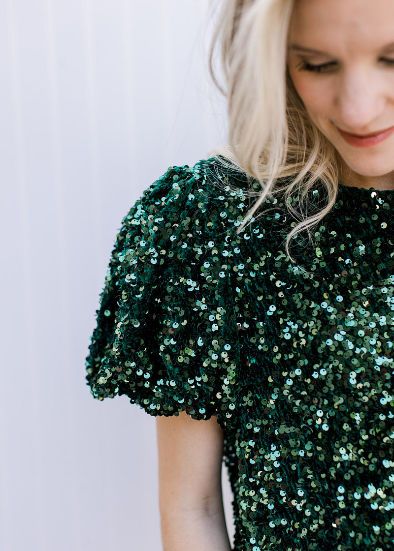 Close up on pleated shoulders and short puff sleeves on an emerald green sequin top. 