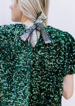 Close up of shimmer tie closure on an emerald green sequin top with short puff sleeves.