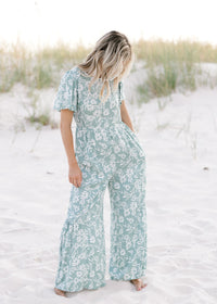 Model wearing a sage jumpsuit with white floral pattern, short sleeves and a smocked detail at waist