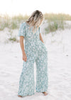 Model wearing a sage jumpsuit with white floral pattern, short sleeves and a smocked detail at waist