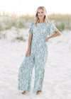 Model wearing a wide leg sage jumpsuit with white floral pattern and short sleeves. 