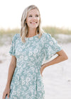 Close up view of smocked detail at waist and short sleeves on a sage jumpsuit with white floral. 