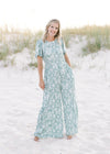 Model wearing a wide leg sage jumpsuit with white floral pattern with a smocked detail at the waist.
