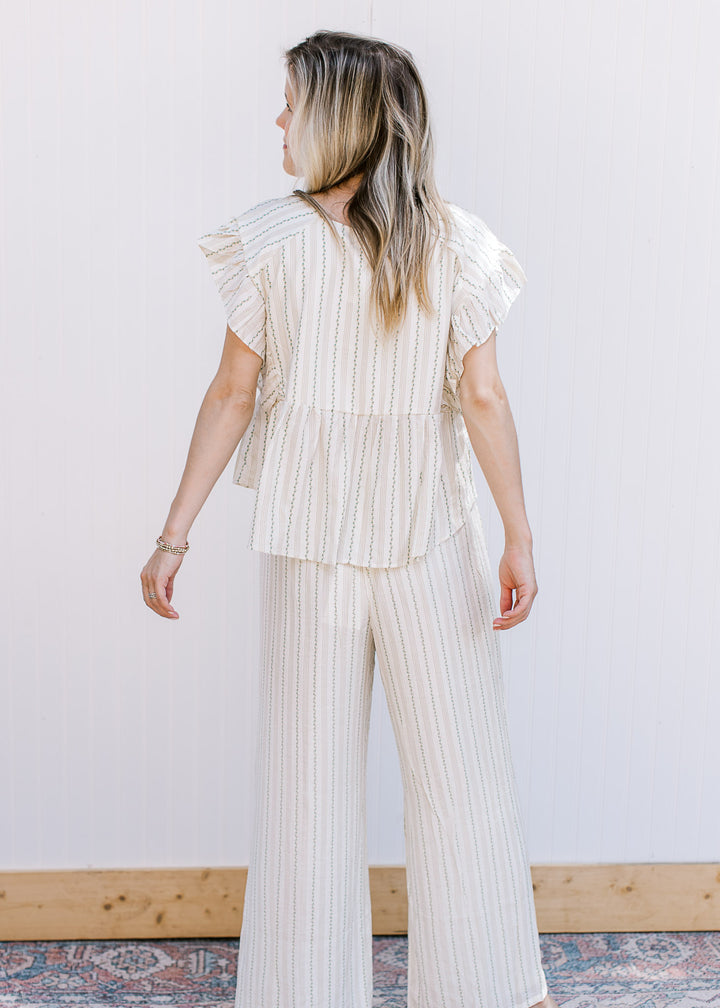 Back view of model wearing a lightweight cream set with green and tan pin stripes and a loose fit. 