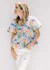 Model wearing white jeans and a sleeveless mustard yellow v-neck top with a cream floral pattern. 