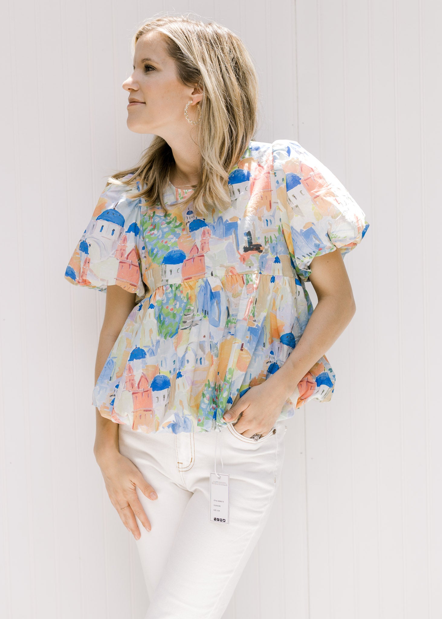 Model wearing white jeans and a sleeveless mustard yellow v-neck top with a cream floral pattern. 