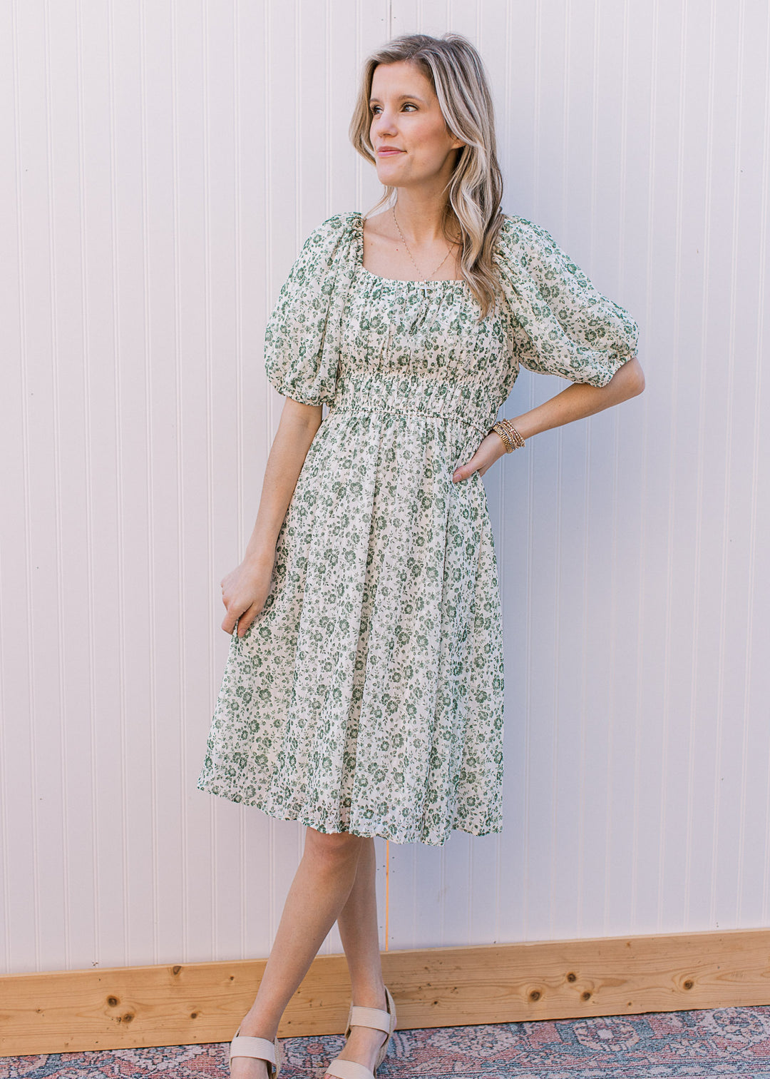 Model wearing a white knee length dress with green floral, square neck and bubble short sleeves.