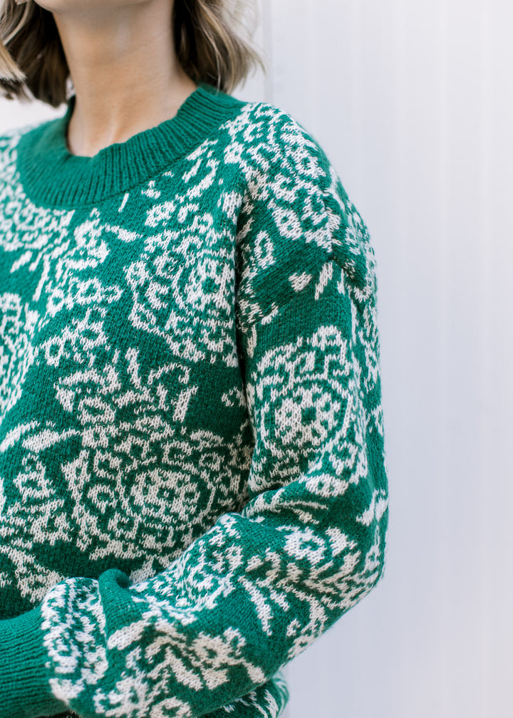Model wearing an evergreen sweater with off-white floral, long sleeves and ribbed evergreen trim.
