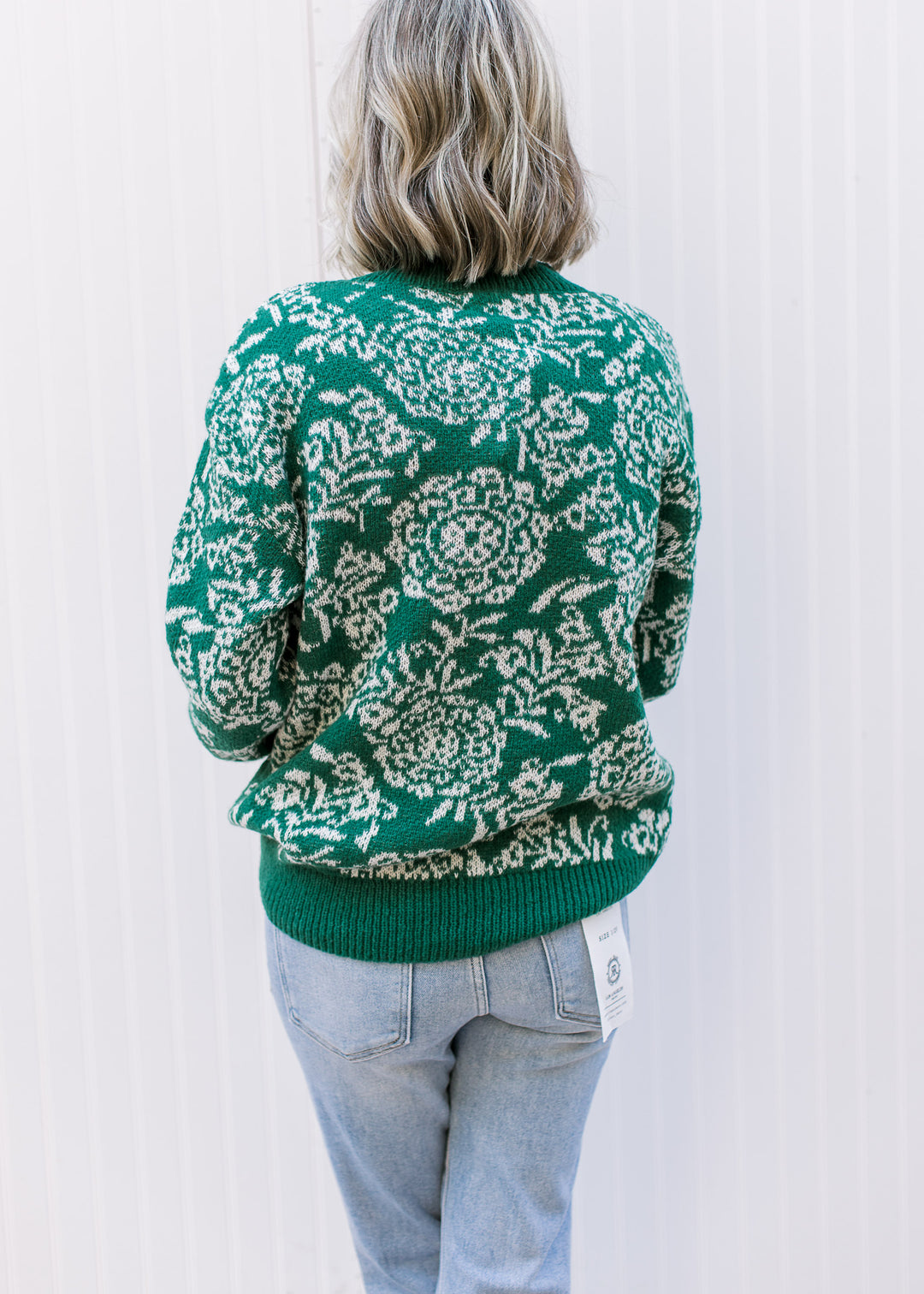 Back view of Model wearing a long sleeve evergreen sweater with off-white floral and evergreen trim.