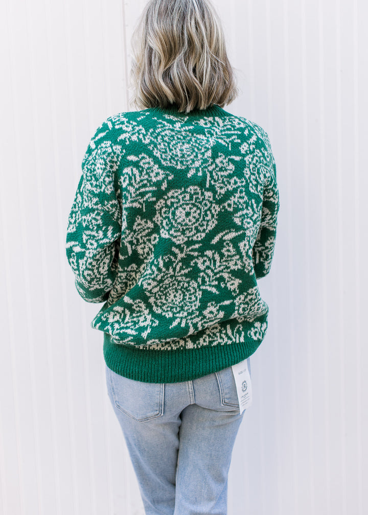 Back view of Model wearing a long sleeve evergreen sweater with off-white floral and evergreen trim.