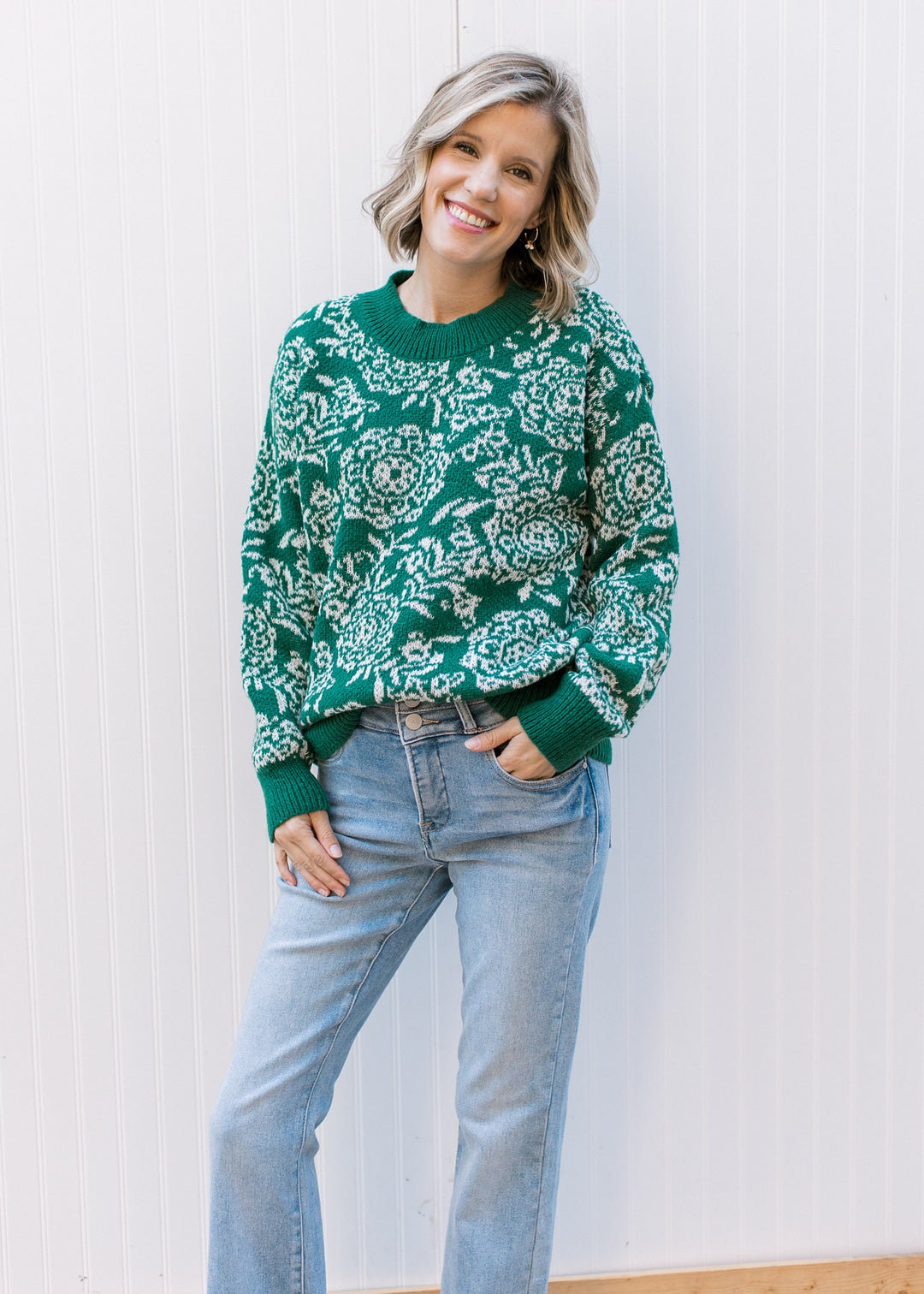 Model wearing a polyester evergreen sweater with off-white floral, long sleeves and evergreen trim.