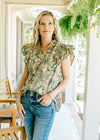 Model wearing jeans with a beige top with green floral, ruffle cap sleeves and a v-neck. 