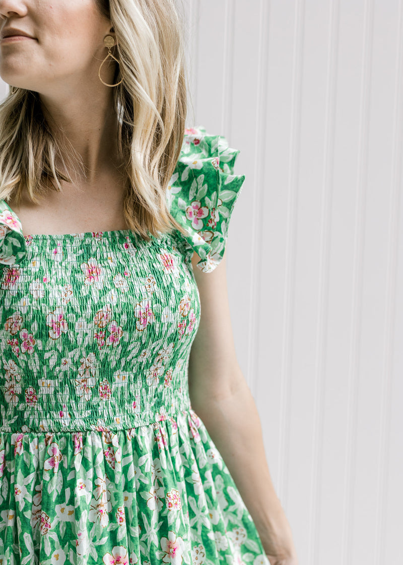 Close up of a smocked bodice and layered sleeveless ruffles on a green dress with  pink floral. 
