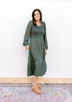 Model wearing an evergreen dress with bubble long sleeves, square neck and brown clogs.