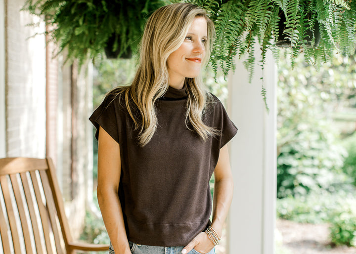 Model wearing a mocha slightly cropped sweater with extended sleeves and a mock neck.  
