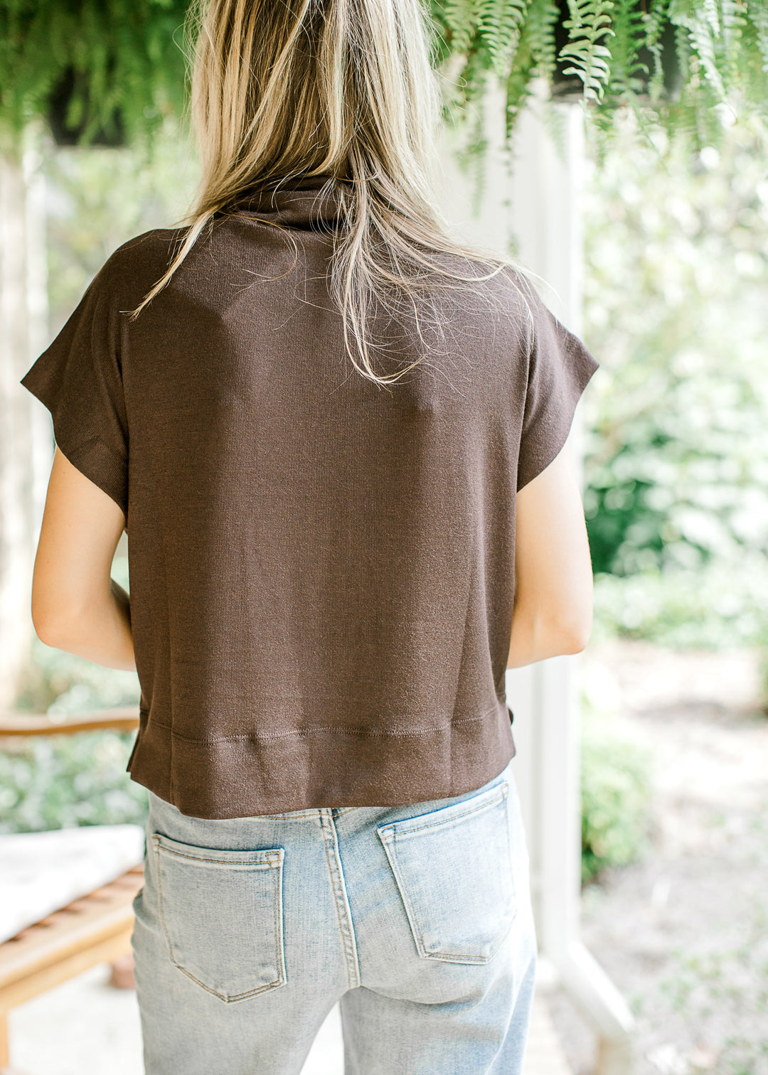 Back view of Model wearing a mocha lightweight sweater with extended sleeves and a mock neck.  