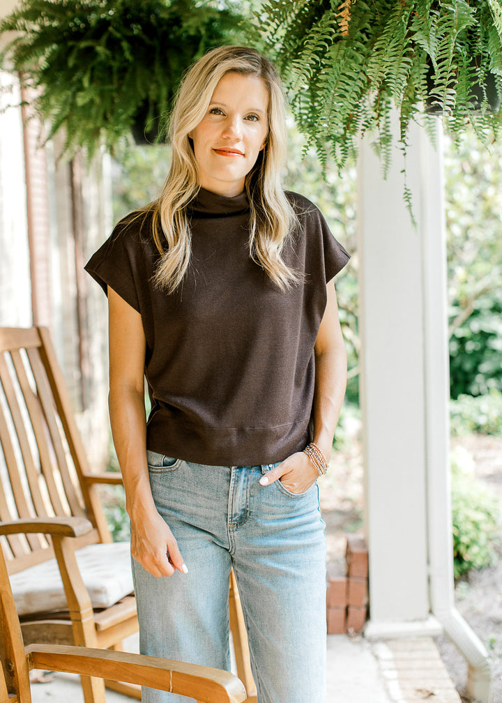 Model wearing jeans and a mocha sweater with extended sleeves and a mock neck.  