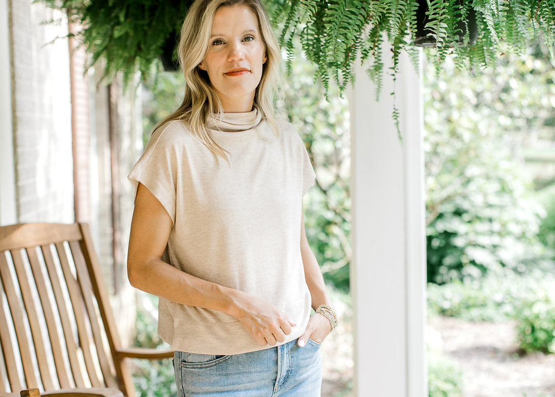 Model wearing an oatmeal sweater with extended sleeves, cropped fit and a mock neck.  